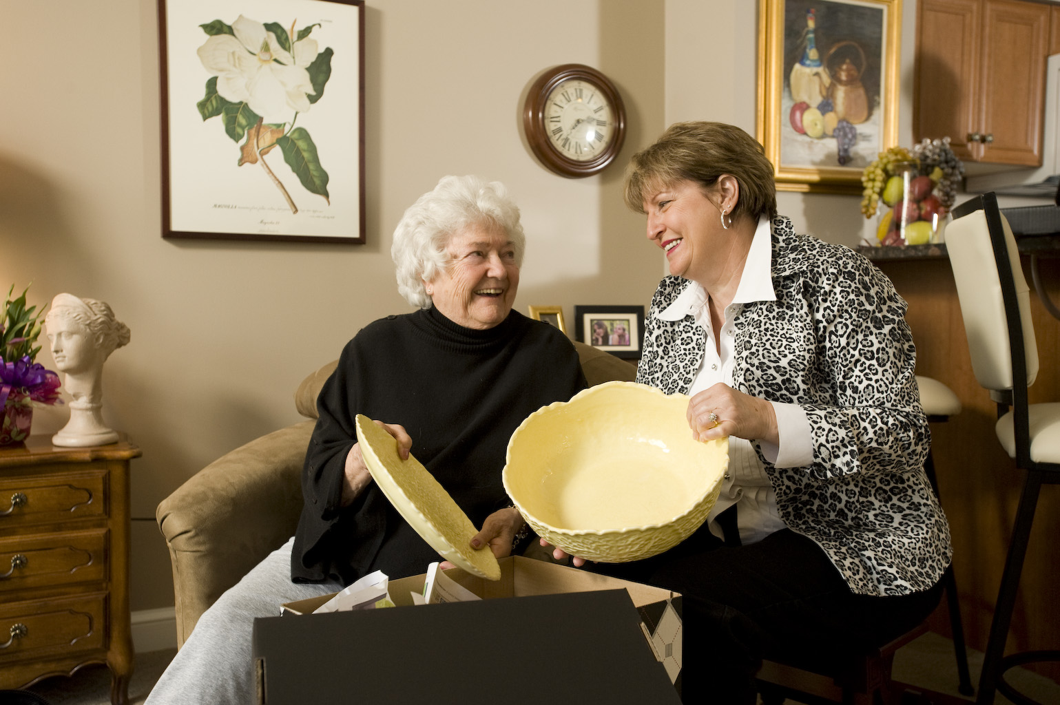 Two senior ladies laughing in a retirement or long term care room looking at a gift. They look happy