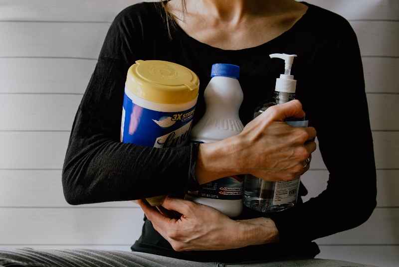 A woman is holding cleaning supplies such as Lysol, bleach and sanitizer